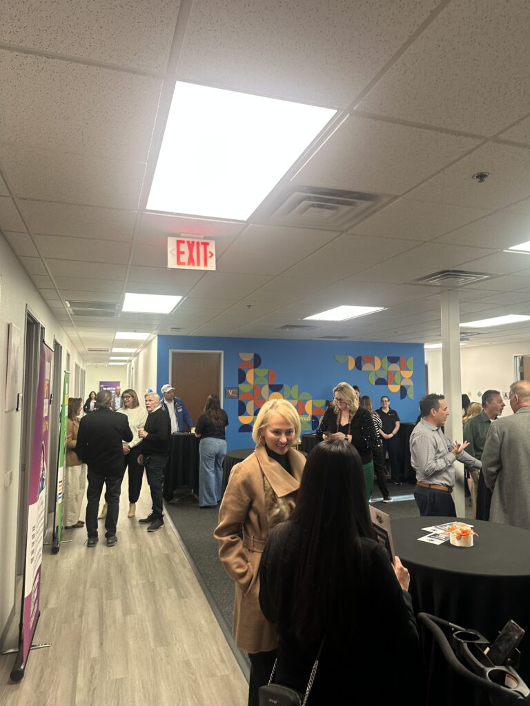 Guests socializing in the hallway of the Grant a Gift Autism Foundation – Ackerman Center interior during the open house event, with blue accent walls and recessed lighting visible