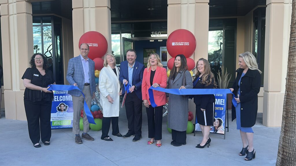 Community members and officials cutting a blue ribbon at a Grant a Gift Autism Foundation event outside a building entrance